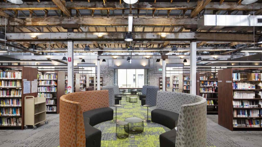 A modern library in Sydney with upgraded lighting, industrial-style ceilings, and comfortable reading areas, showcasing improved electrical infrastructure.